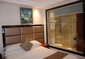 Hotelkamer met een groot bed, hoofdeinde, schilderij aan de muur en een douchecabine van glas.