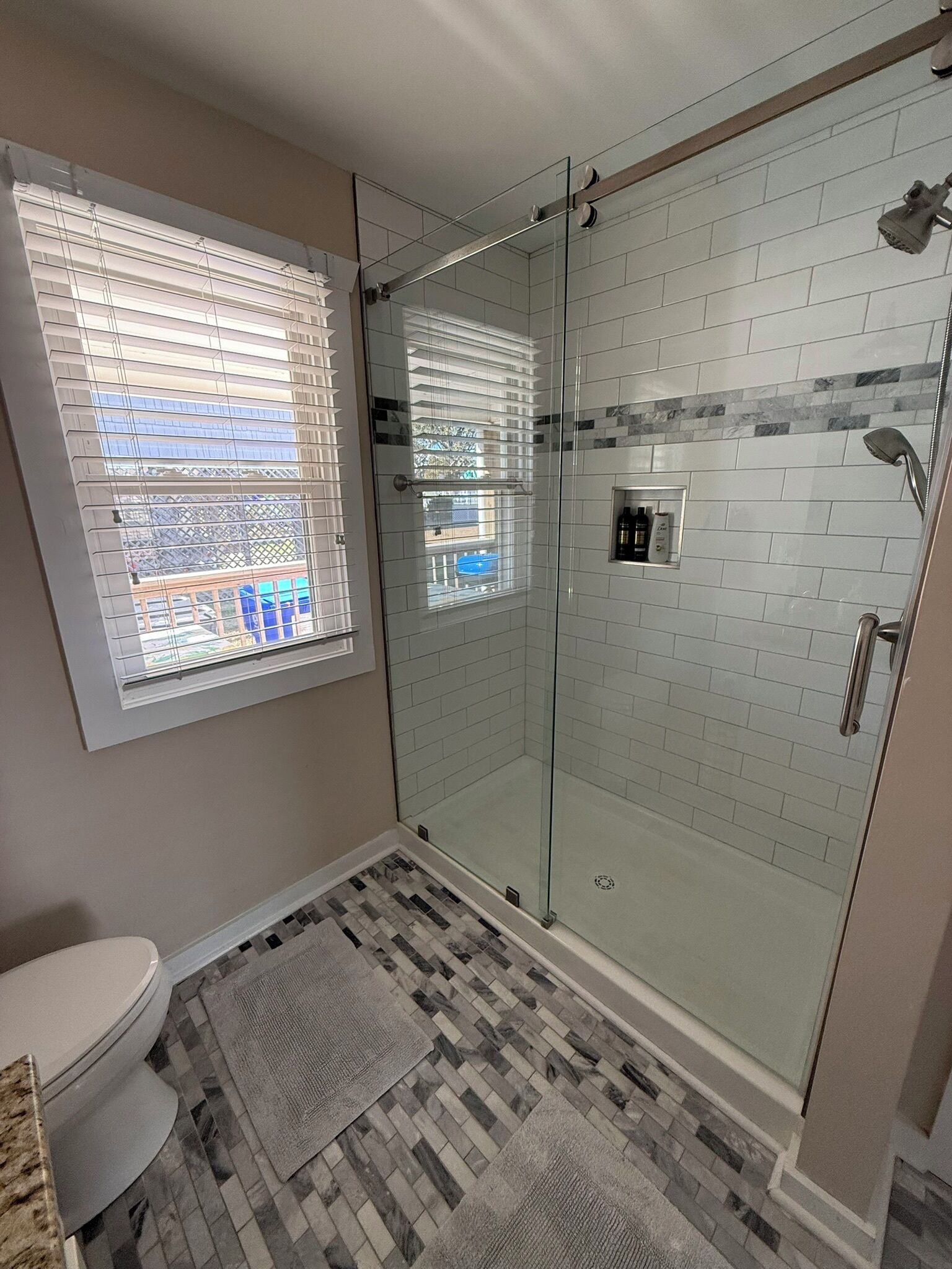 Un baño moderno con ducha de vidrio, inodoro y ventana con persianas.