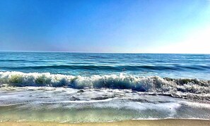 A beach with waves crashing onto the shore under a clear sky. - Oak Island Beach House -- Sand, Sun, and Fun Just Steps Away!! (Oak Island)