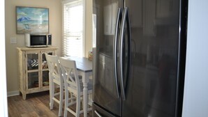 A kitchen with a stainless steel refrigerator, a microwave, and a dining table with chairs. - Oak Island Beach House -- Sand, Sun, and Fun Just Steps Away!! (Oak Island)