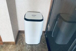 A white trash bin with a black lid labeled "mini" in a corner of a room with tiled flooring. - Yazhi Hotel (Qingyang)