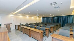 Un salón de conferencias con filas de sillas, un atril y un proyector en el techo.