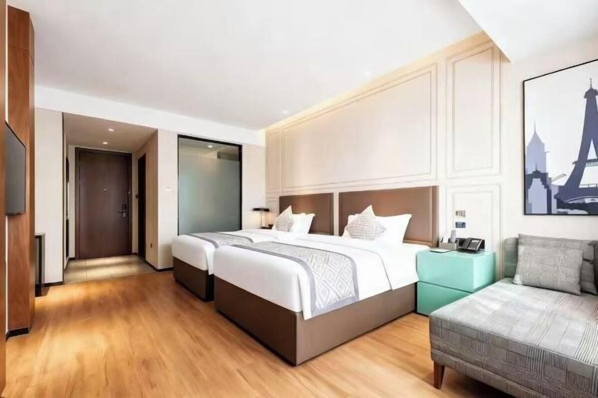 A hotel room with a large bed, a sofa, a TV, and a painting of a cityscape.