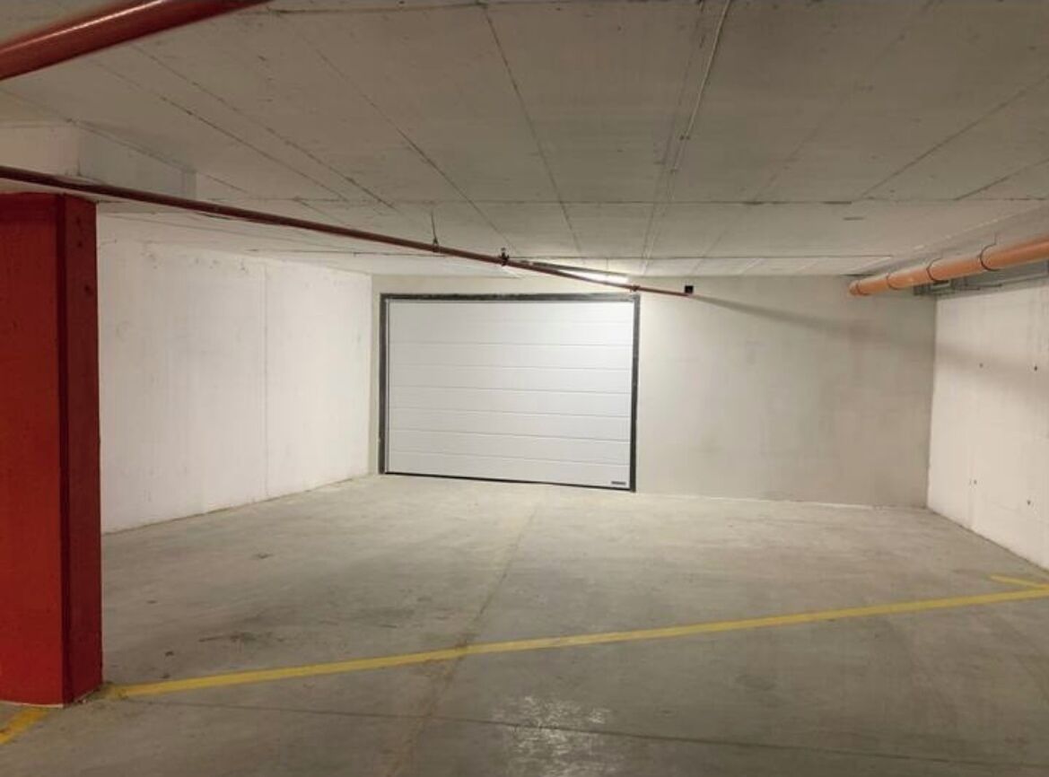 Un pàrcing subterrani amb una porta tancada, sòl de formigó i línies pintades de color groc per indicar els aparcaments.