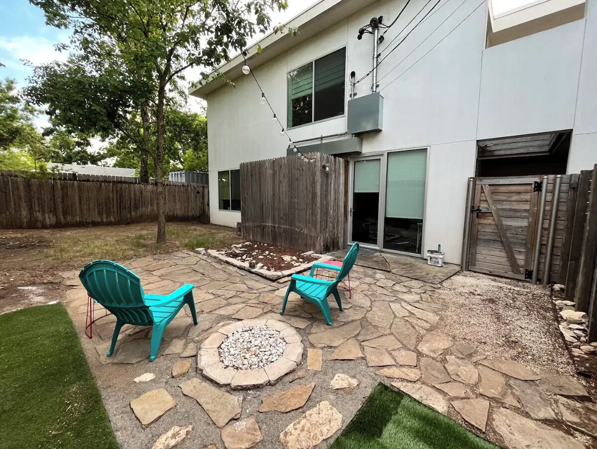 Un patio trasero con dos sillas turquesas, un hogar de piedra y una valla de madera.