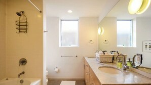 A modern bathroom with a bathtub, a shower, a vanity with a sink, and a large mirror. - Sun Filled Haus: Private Entry, Yard, Carport (Austin)