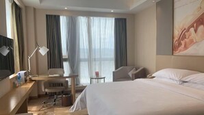 Ein Hotelzimmer mit Bett, Schreibtisch, Stuhl, einem kleinen Tisch und einem Fenster mit Vorhängen.