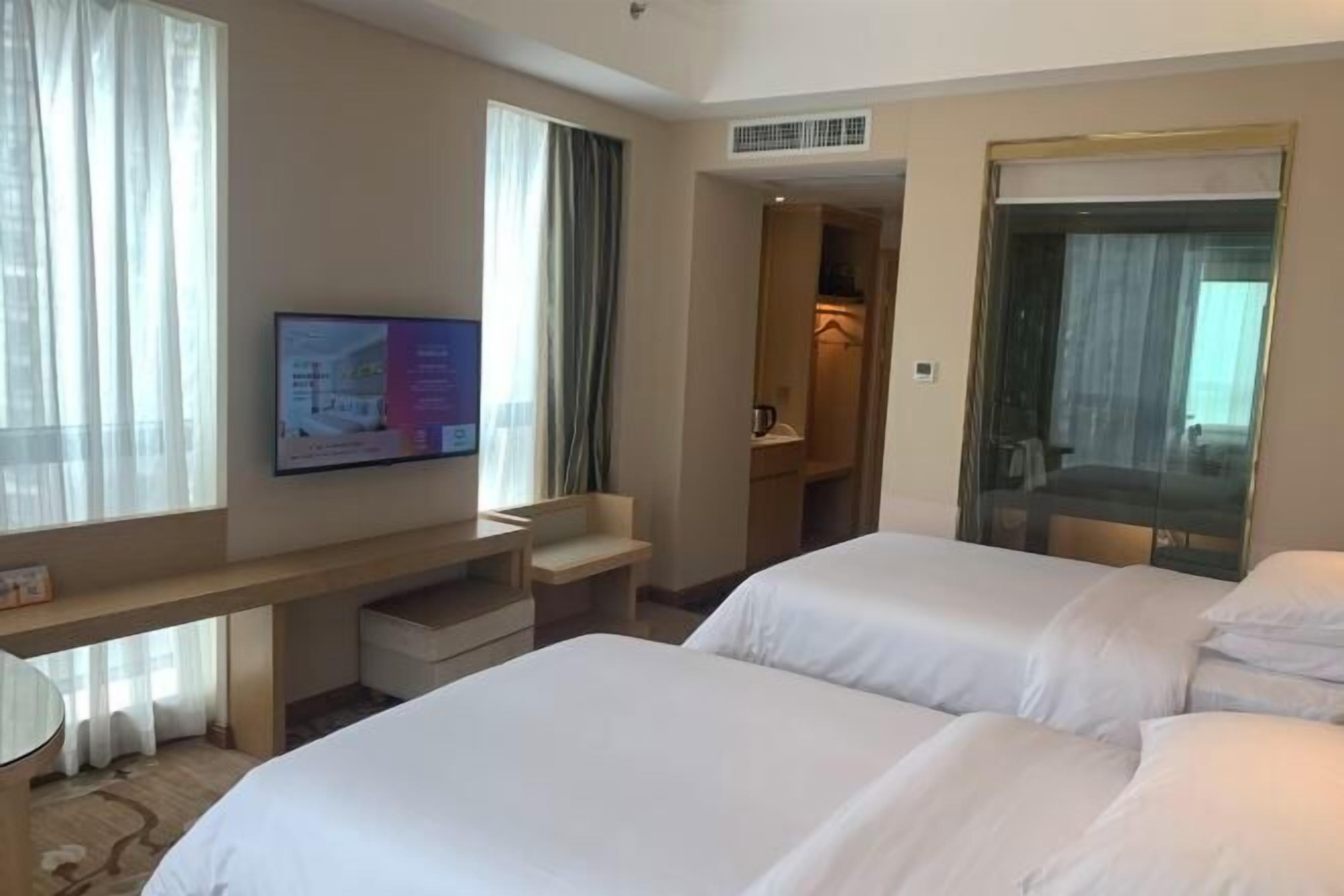 A hotel room with two beds, a TV mounted on the wall, a desk, and a walk-in closet.