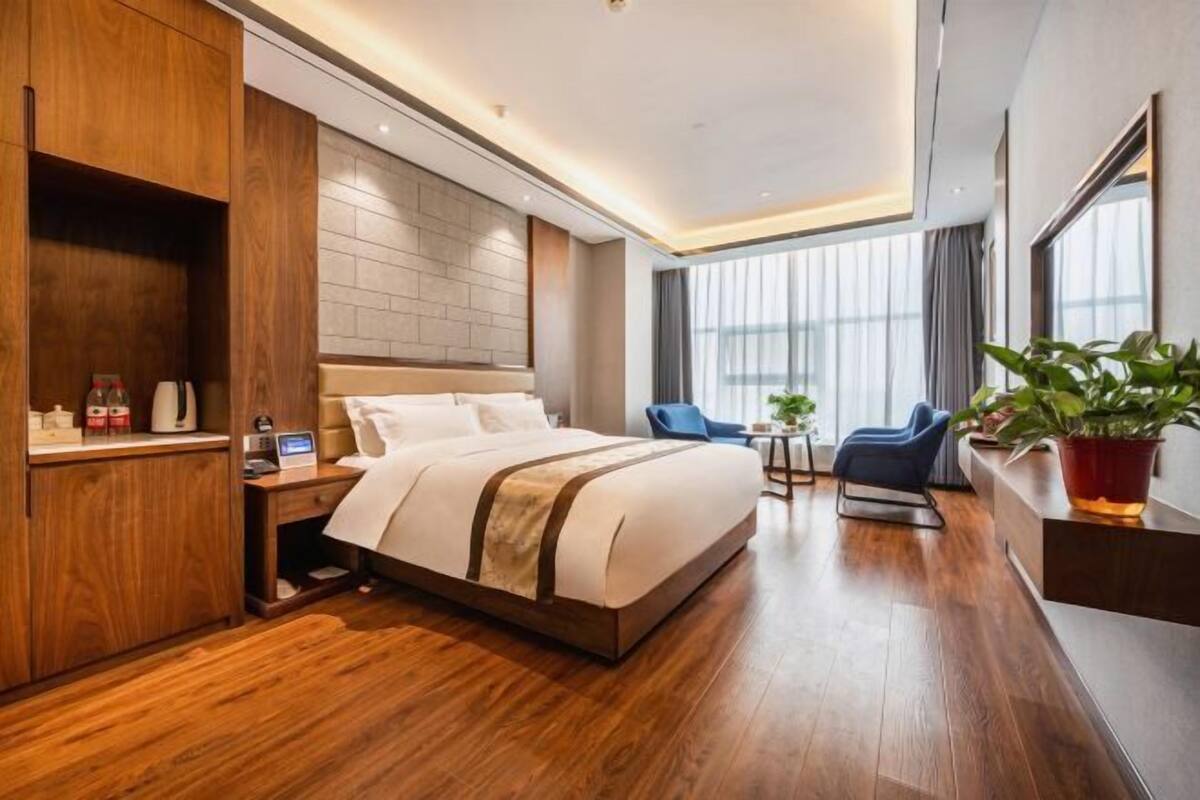 Una habitación de hotel moderna con una cama grande, suelo de madera, un escritorio con una computadora portátil, una silla y una planta en maceta.