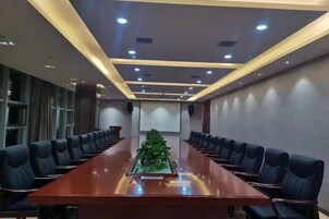 Un salón de conferencias con una larga mesa, sillas, una pantalla de proyector y un centro de mesa con planta.