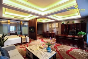 A hotel room with a bed, a desk, a chair, a table with a vase, and a carpet with a red and white pattern.