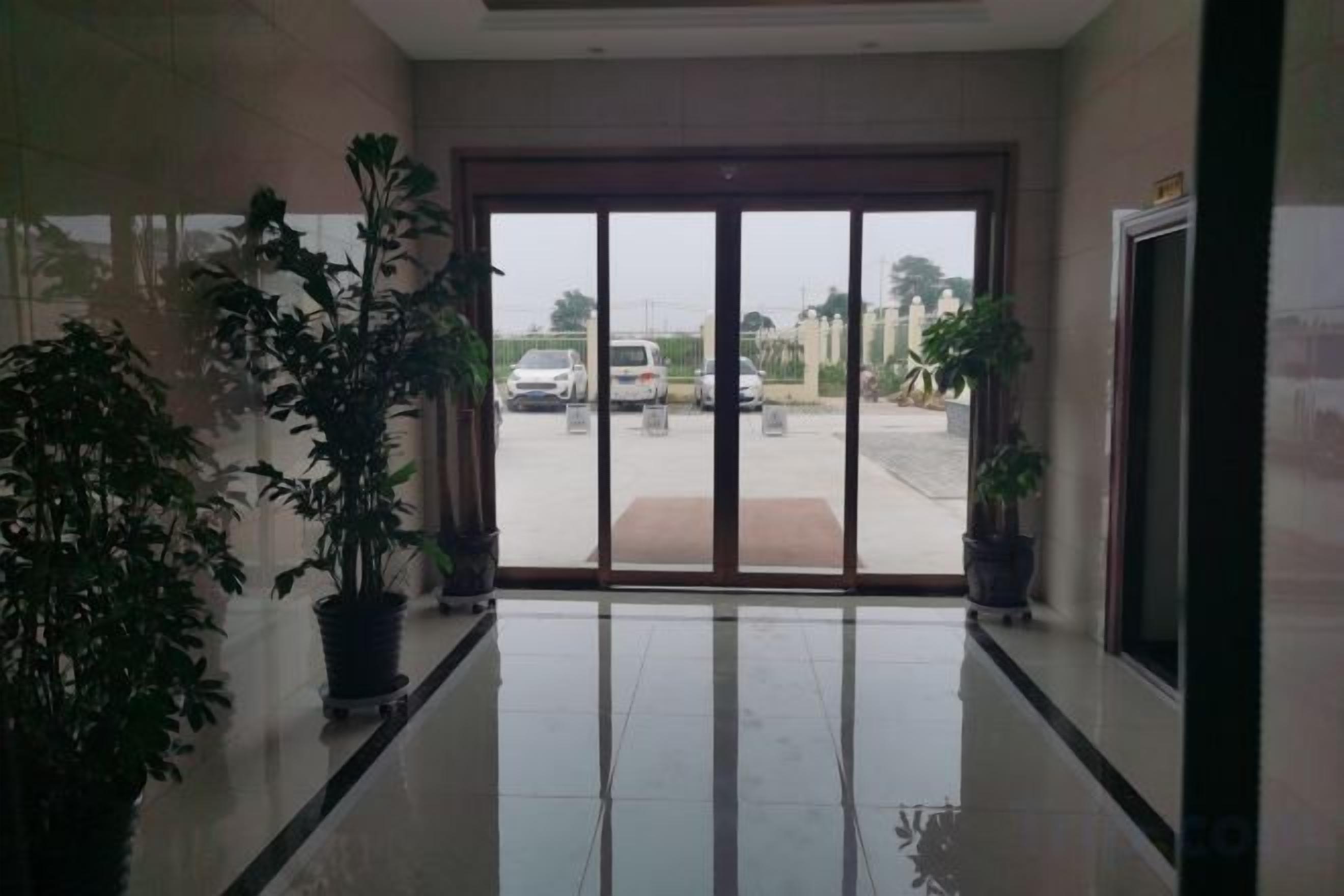 Un hall de hotel con un gran ventanal que da a un estacionamiento. Hay plantas en macetas a ambos lados de la puerta.