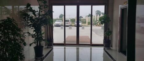 Un hall de hotel con un gran ventanal que da a un estacionamiento. Hay plantas en macetas a ambos lados de la puerta.