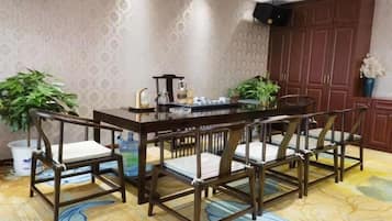 A dining area with a wooden table and chairs, potted plants, and a patterned carpet.