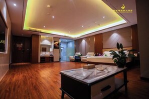 Een moderne hotelkamer met een houten vloer, een marmeren salontafel, een bed met hoofdeinde, een zithoek met een bank en fauteuils, en een klein balkon met een bloempot.