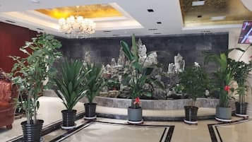 A lobby with a reception desk, potted plants, a chandelier, and a decorative wall.