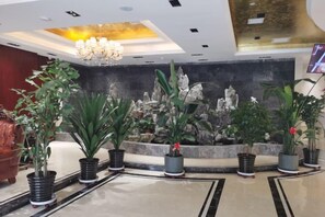 Un hall d’entrée avec un comptoir de réception, des plantes en pot, un lustre et un mur décoratif.