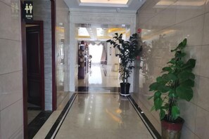 Een hotelgang met een potplant, een bordje dat de herentoiletten aangeeft, en een weerspiegeling van het interieur op de gepolijste vloer.