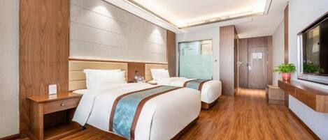 A hotel room with two beds, wooden flooring, a large mirror, and a potted plant.
