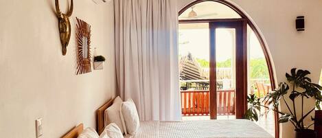 A hotel room with two beds, a ceiling fan, a view of the outside, and a plant.
