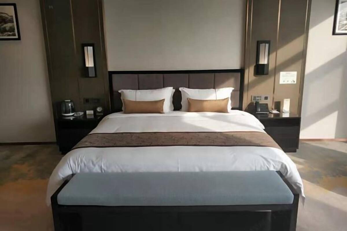 Habitación de hotel con una cama grande, una mesita de noche y una lámpara de pared.