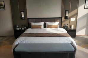 A hotel room with a large bed, a bedside table, a nightstand, and a wall-mounted light fixture.