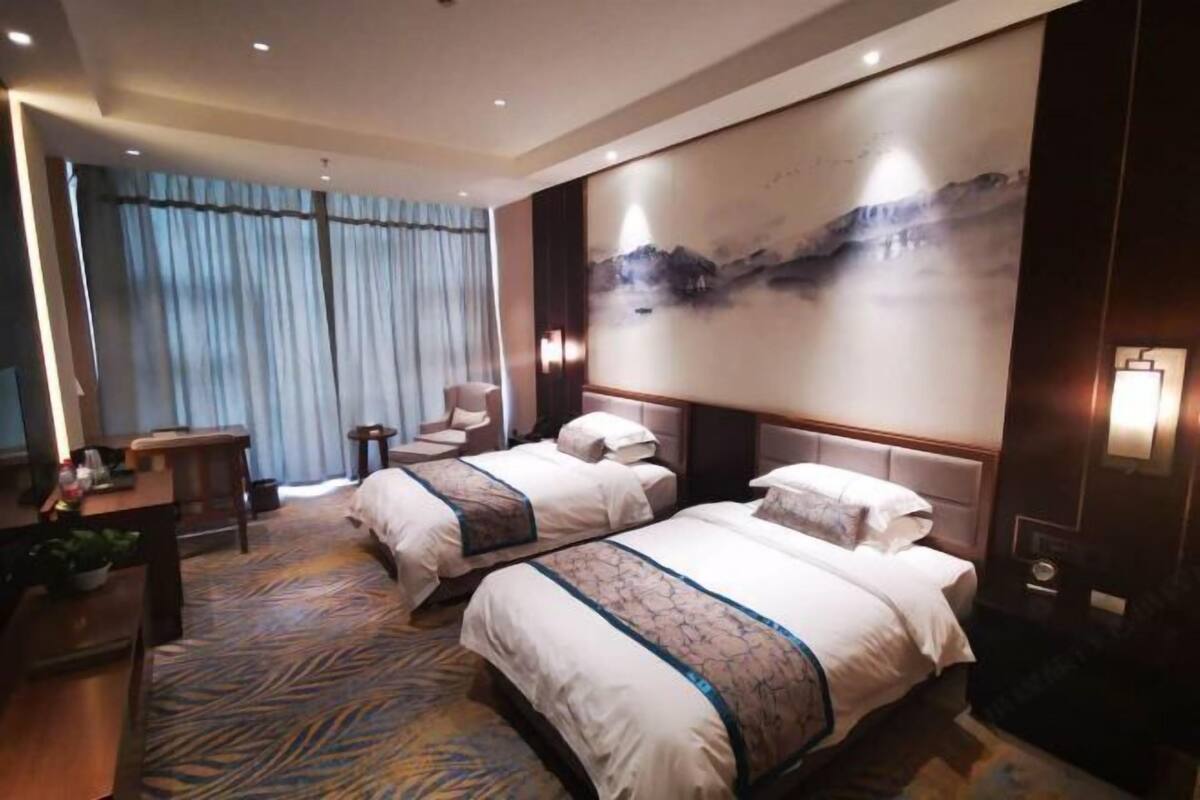 Habitación de hotel con dos camas, un escritorio, una silla, un cuadro grande y una ventana con cortinas.