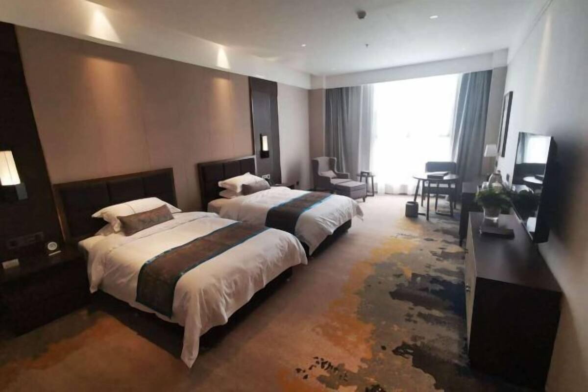 Habitación de hotel con dos camas, un escritorio, una silla, un televisor y un ventanal grande.
