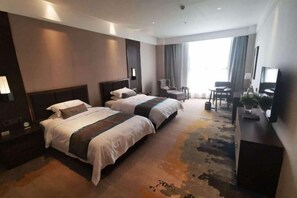 A hotel room with two beds, a desk, a chair, a TV, and a large window.