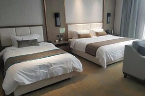 A hotel room with two beds, a sofa, and a nightstand with a lamp.