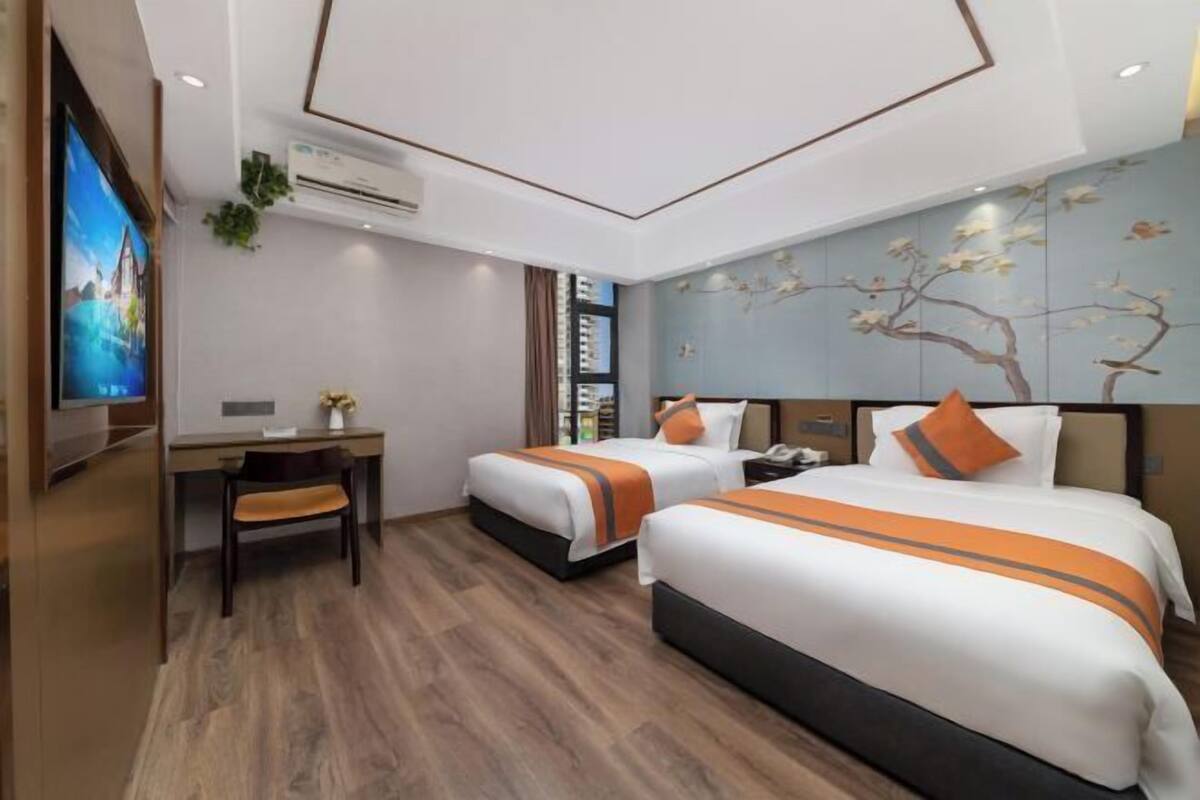 A hotel room with two beds, a desk, and a TV.