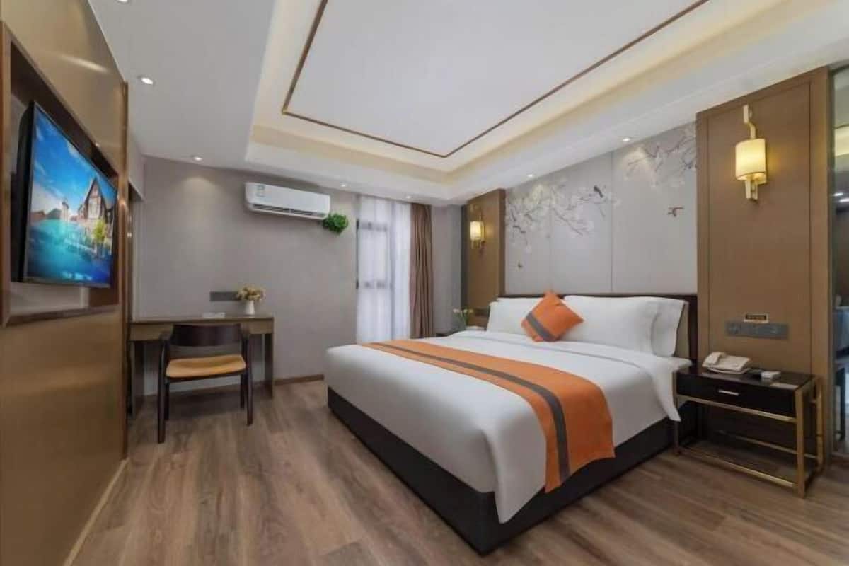 A hotel room with a bed, desk, chair, and a TV on the wall.