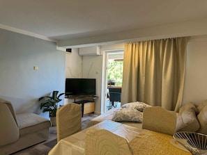 A living room with a sofa, a television, a dining table, and a potted plant. - Holiday apartment with balcony and pool (Jadranovo)