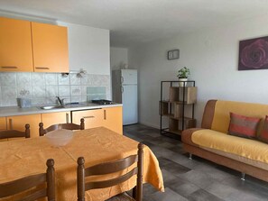 A compact kitchen with a dining table and chairs, a sofa, and a small plant on a shelf. - Holiday apartment with a view and pool (Jadranovo)