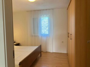 A bedroom with a bed, a window with sheer curtains, a wardrobe, and a bedside table. - Holiday apartment with a view and pool (Jadranovo)