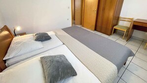 A bedroom with two beds, a wooden wardrobe, a desk, and a chair.
