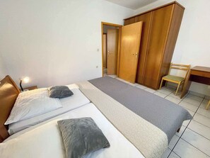 A bedroom with two beds, a wooden wardrobe, a desk, and a chair.