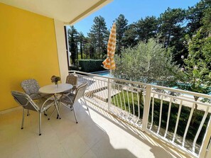 Varanda com mesa e cadeiras, piscina e vegetação ao redor.