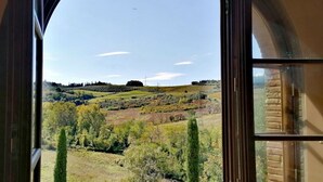 A view through a window of a landscape with rolling hills, trees, and a clear sky. - La Quercia, apartment with garden for 6/8 people  in the heart of Chianti (Montespertoli)