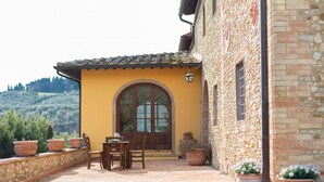 A stone building with a yellow facade, a wooden door, and a patio with a table and chairs. - La Quercia, apartment with garden for 6/8 people  in the heart of Chianti (Montespertoli)