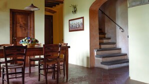 A dining area with a wooden table and chairs, a hanging light fixture, a framed picture on the wall, and a staircase with stone steps. - La Quercia, apartment with garden for 6/8 people  in the heart of Chianti (Montespertoli)