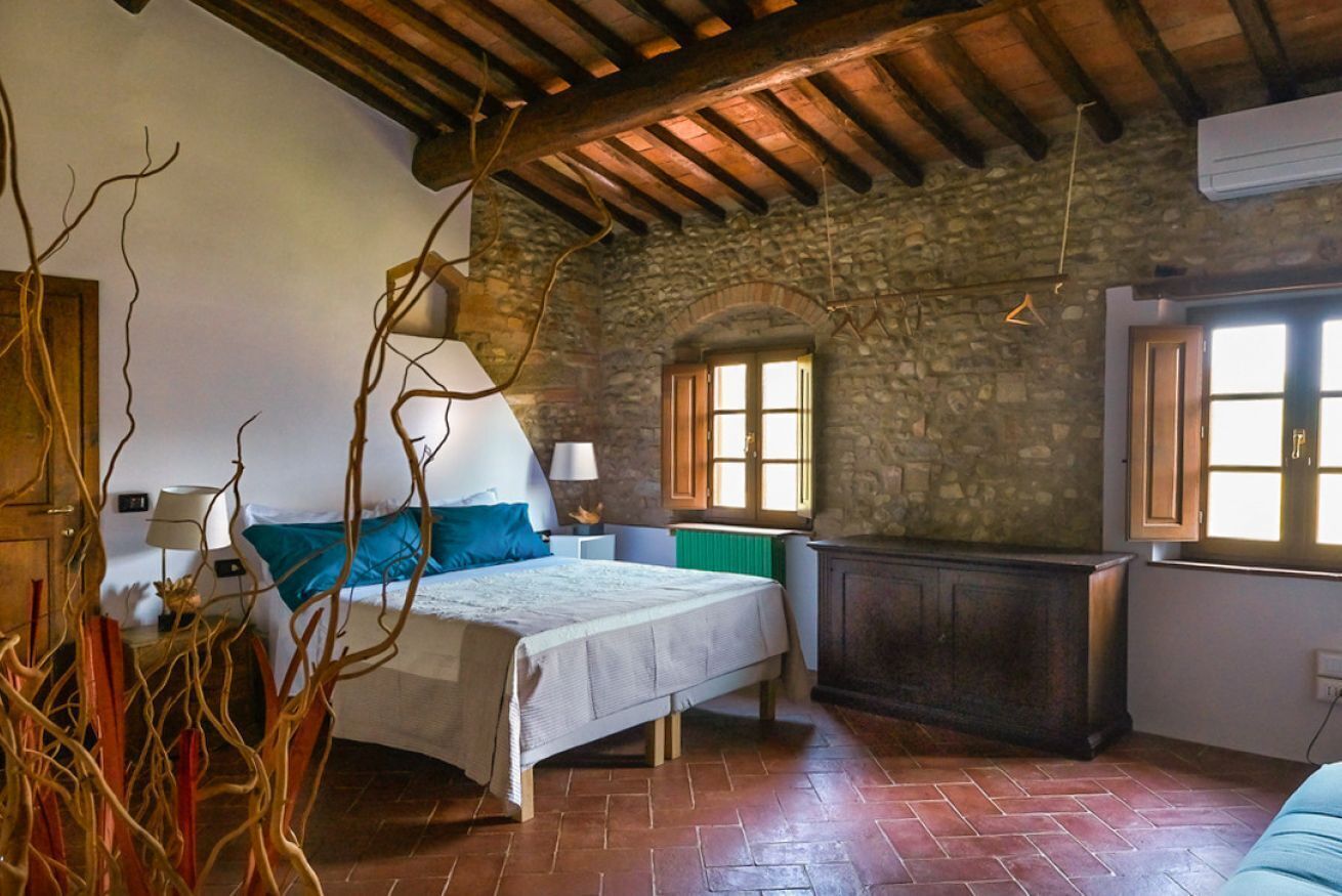 Una camera da letto con un letto, un comodino, una cassettiera e un muro in pietra.