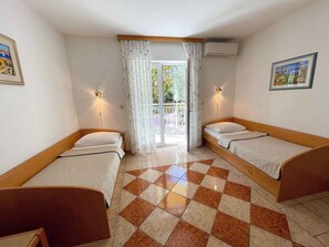 A room with two beds, a checkered floor, and a balcony with curtains.