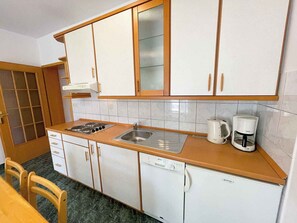 A compact kitchen with white cabinets, a sink, a stove, a dishwasher, and a coffee maker.