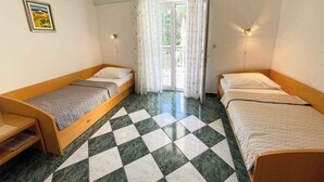A room with two single beds, a small table, and a window with curtains. - Holiday apartment with outdoor swimming pool (Jadranovo)