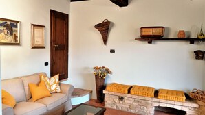 Un salon comprenant un canapé, une table basse, une cheminée, une étagère murale décorée de divers objets, et une porte.