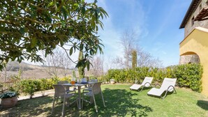 Une terrasse avec une table et des chaises, un petit arbre et un bâtiment à la façade jaune.