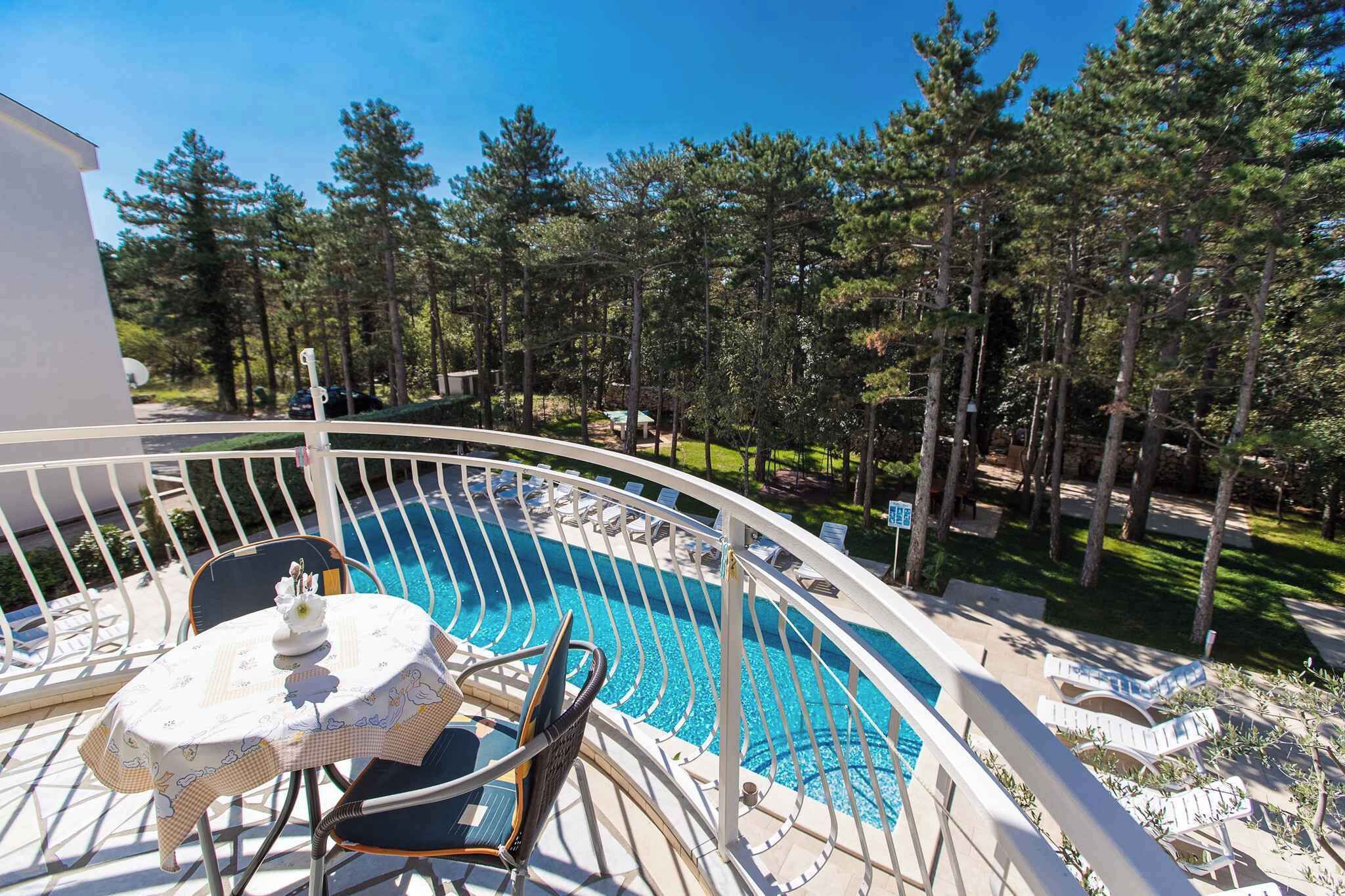 A pool area with a curved white railing, a table with chairs, and a view of a forested area.