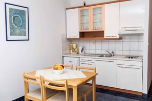 Una cocina compacta con armarios blancos, una cafetera y un frutero sobre la mesa.