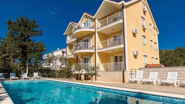 Ein mehrstöckiges Hotel mit Schwimmbad, Balkonen und Liegestühlen.